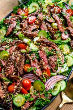 steak salad with tomatoes, cucumbers and onions in a black bowl on a wooden table