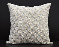 a white pillow with pearls on the front and back, sitting on a black surface