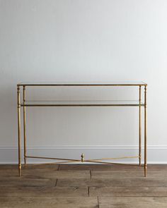 a gold metal and glass console table against a white wall in an empty room with wood flooring