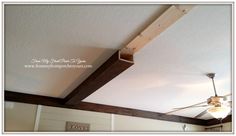 a ceiling fan is mounted to the side of a wooden beam in a room with white walls