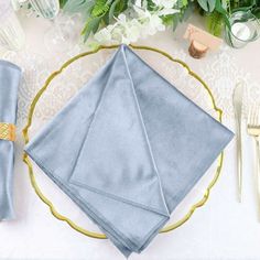 a place setting with blue napkins and silverware on a gold rimmed plate