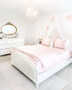 a white bed with pink comforter and pillows in a small room next to a chandelier