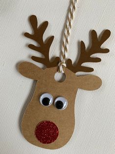 a paper reindeer ornament hanging from a string on a white wall with red glitter eyes