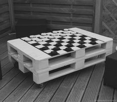 a table made out of pallets with chess pieces on it and two chairs in the background