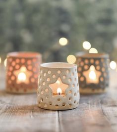 three lit candles sitting on top of a wooden table next to some lights in the background