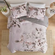 a bed with pink and grey flowers on the comforter, pillows and pillow cases