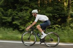 a man riding a bike down a street next to lush green trees in the background