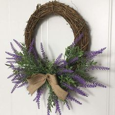 a wreath hanging on the door with purple flowers and burlock tied around it