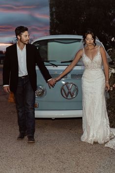 a bride and groom holding hands in front of a vw camper van at sunset