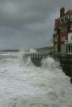 large waves crashing into the shore in front of a red brick building on a stormy day