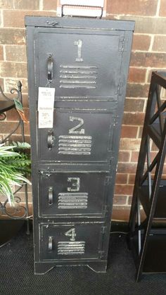 a metal filing cabinet sitting next to a plant in front of a brick wall with numbers on it