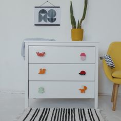 a white dresser sitting next to a yellow chair in a room with a potted plant