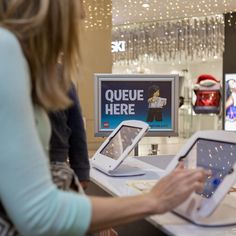 two women at a store looking at electronic devices in front of a sign that says queue here