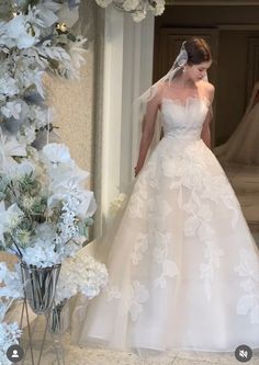 a woman in a wedding dress walking down a hall with white flowers on the floor