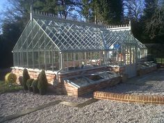 a large glass house sitting in the middle of a gravel area next to trees and bushes