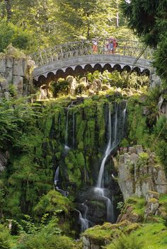 a waterfall with a bridge over it and people standing at the top on one side