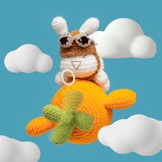 a crocheted stuffed animal is flying through the air with clouds in the background