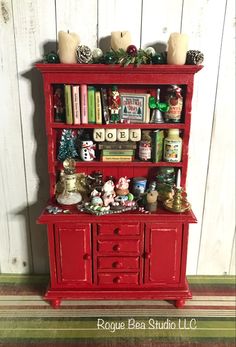 a red china cabinet with christmas decorations on top and bookshelf above it, against a white painted wood wall