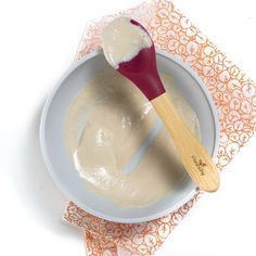 a wooden spoon is in a bowl of cream and sits on an orange doily