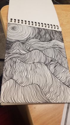 a spiral notebook with black and white lines on it sitting on top of a wooden table