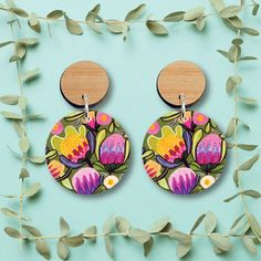 a pair of earrings with flowers painted on them and wooden discs hanging from the back