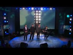 three men standing on a stage in front of televisions with lights shining down them