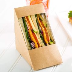 a sandwich in a brown paper box on a white table with orange slices and lettuce