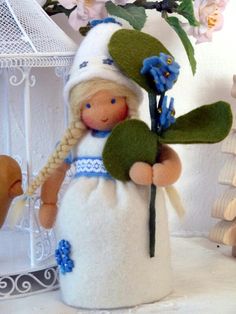 a doll holding a flower in her hand and wearing a white dress with blue flowers