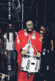 a man in a red outfit is holding a drum and some people are standing behind him