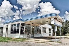 an old gas station sitting on the side of a road with clouds in the sky