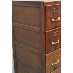 an old wooden file cabinet with three drawers and brass pulls on the bottom, against a white wall