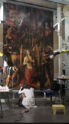 a man sitting on the floor in front of a large painting with people around it