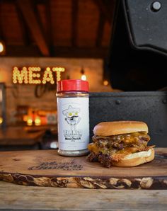 a meat sandwich sitting on top of a wooden cutting board next to a jar of bbq sauce