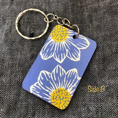 a blue and yellow keychain with white daisies on it, sitting on a gray cloth