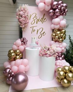 a pink and gold bridal to be sign surrounded by balloons, flowers and vases