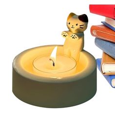 a candle that is sitting next to some books and a cat figurine on top of it