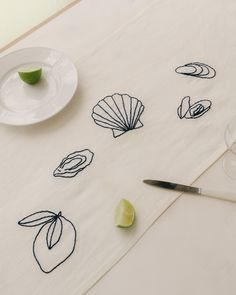 a white table topped with a plate and knife next to a glass filled with limes