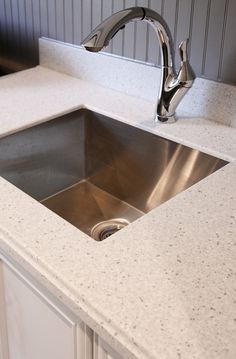 a kitchen sink with a faucet in the middle and marble countertops on both sides