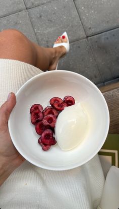 a person holding a white bowl with strawberries in it and yogurt on top