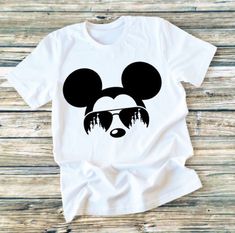 a white shirt with a mickey mouse face and sunglasses on it's head, against a wooden background