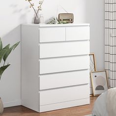 a white dresser sitting next to a bed in a bedroom on top of a hard wood floor