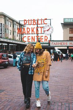 two people are walking down the street in front of a market center sign that says public market center