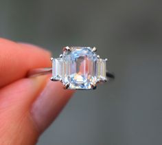 a person holding an engagement ring with three stones on it's side and the center stone in the middle