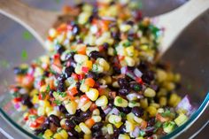 a glass bowl filled with black beans, corn and vegtables next to a wooden spoon