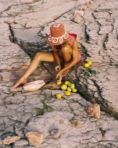 a woman is sitting on the ground with fruit in her hand and wearing a hat