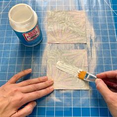 two hands are holding a paintbrush and painting the fabric on a piece of paper