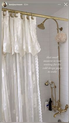 the shower curtain is white and has gold hardware on it, along with an antique brass faucet