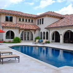 an outdoor swimming pool with lounge chairs and umbrellas next to the home's patio