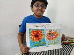 a young boy holding up a coloring book with pictures of flowers on it in front of him