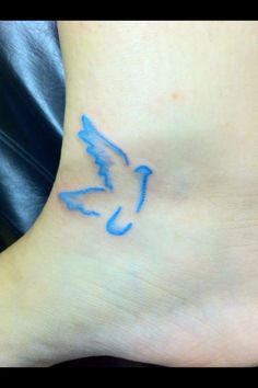 a small blue bird tattoo on the side of a woman's foot, with an arrow drawn across it